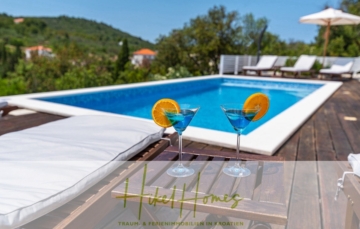 Zwei blaue Cocktails mit Orangenscheiben stehen auf einem Holztisch neben einem Pool. Der Poolbereich verfügt über weiße Liegen und Sonnenschirme. Im Hintergrund sind Grünflächen und Hügel zu sehen. Der Text lautet „HOME“ mit zusätzlichem Text über Ferienhäuser in Kroatien. - 2 Meerblick Villen + freies Grundstück ideal zur Vermietungauf der Insel Dugi Otok jeweils mit Pool