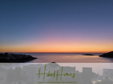 Ein ruhiger Sonnenuntergang über einem ruhigen Meer mit den Silhouetten eines Küstendorfs. Der Himmel wechselt von tiefblau zu orange am Horizont. Der Text „Hikel Homes Traum- & Ferienimmobilien in Kroatien“ ist unten eingeblendet. - Einziehen im Sommer - Meerblick Neubau-Luxusvilla mit Einrichtung, Infinitypool & Raumkonzept