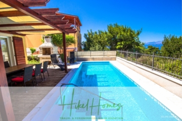 Außenszene mit Swimmingpool, Terrasse und Grillplatz unter einer Pergola. Rote Stühle umgeben einen Esstisch in der Nähe. Grünflächen und Bäume grenzen an den Bereich, mit Blick auf das Meer und einem klaren blauen Himmel im Hintergrund. Branding-Overlay unten. - Villa im Mittelmeerstil mit 3 SZ, Pool, Dachterrasse mit Meerblick – möbiliert (9)