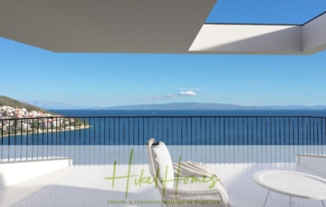 Ein moderner Balkon mit einer eleganten weißen Sonnenliege und einem runden Tisch bietet Ausblick auf ein weites, ruhiges blaues Meer. Der Himmel ist klar und blau und auf der linken Seite ist eine kleine Küstenstadt zu sehen, eingebettet zwischen grünen Hügeln. - Meerblick Penthouse mit außergewöhnlicher Architektur 104m² mit 2 SZ, Terrasse und Südausrichtung