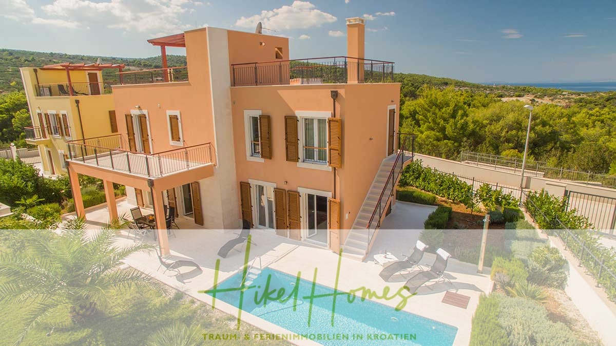 Eine zweistöckige pfirsichfarbene Villa mit Balkonen und Pool, umgeben von Grün. Im Hintergrund sieht man Meer und Hügel. Unten ist der Text „Hike Homes“ eingeblendet. - Villa im Mittelmeerstil mit 3 SZ, Pool, Dachterrasse mit Meerblick (3/4)