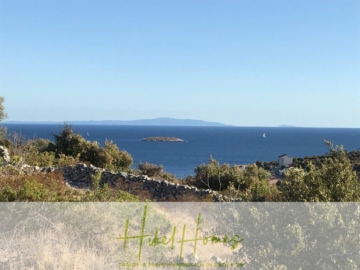 Malerische Aussicht auf eine Küstenlandschaft mit Meer und entfernten Inseln. Büsche und trockenes Gras füllen den Vordergrund, durch die Landschaft verläuft eine Steinmauer. Ein paar Segelboote liegen im Wasser unter einem klaren blauen Himmel. - 805m² Bauland in Panoramahanglage mit traumhaften Rundumblick aufs Meer und die vorgelagerten Inseln